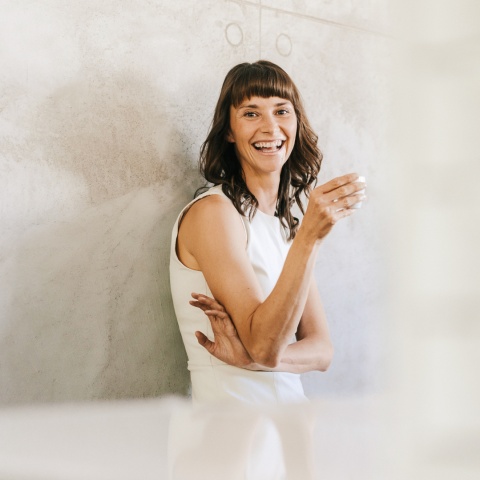 Frau mit Kaffee steht lächelnd an einer Wand - natürliche Farben